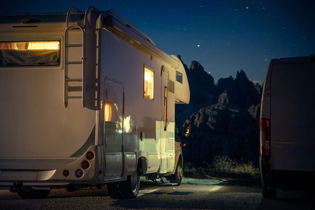 A camper van parked under a night sky full of stars in the mountains.
