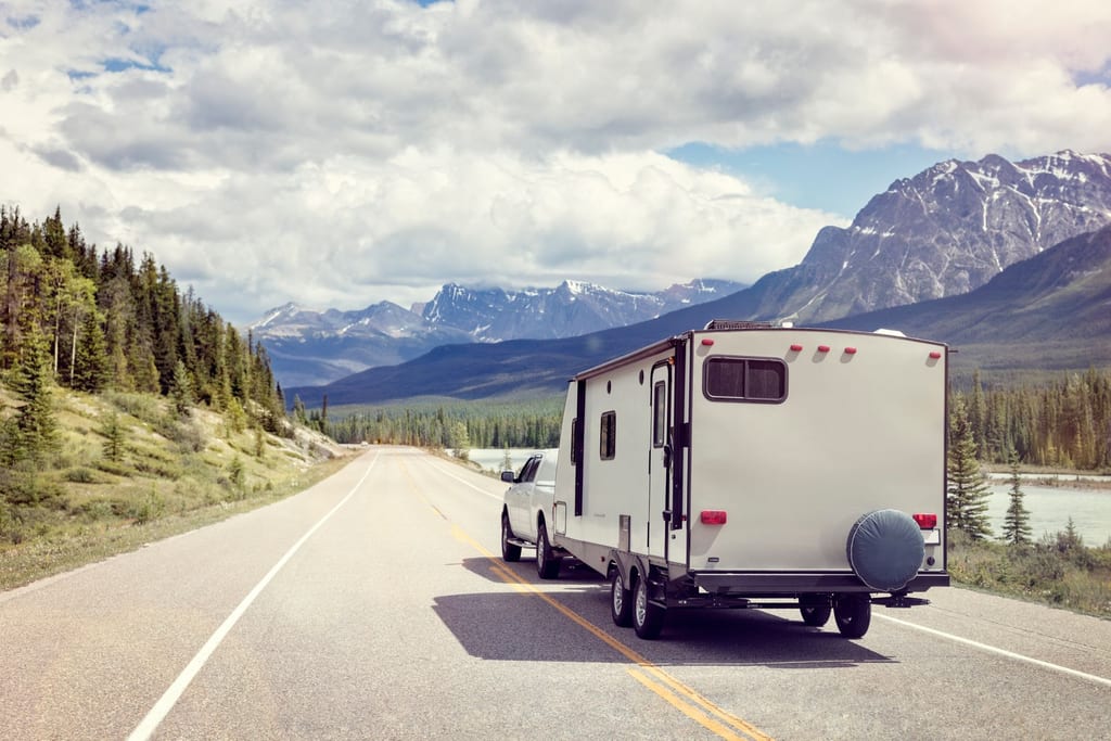 A camper trailer on the road beside a river.