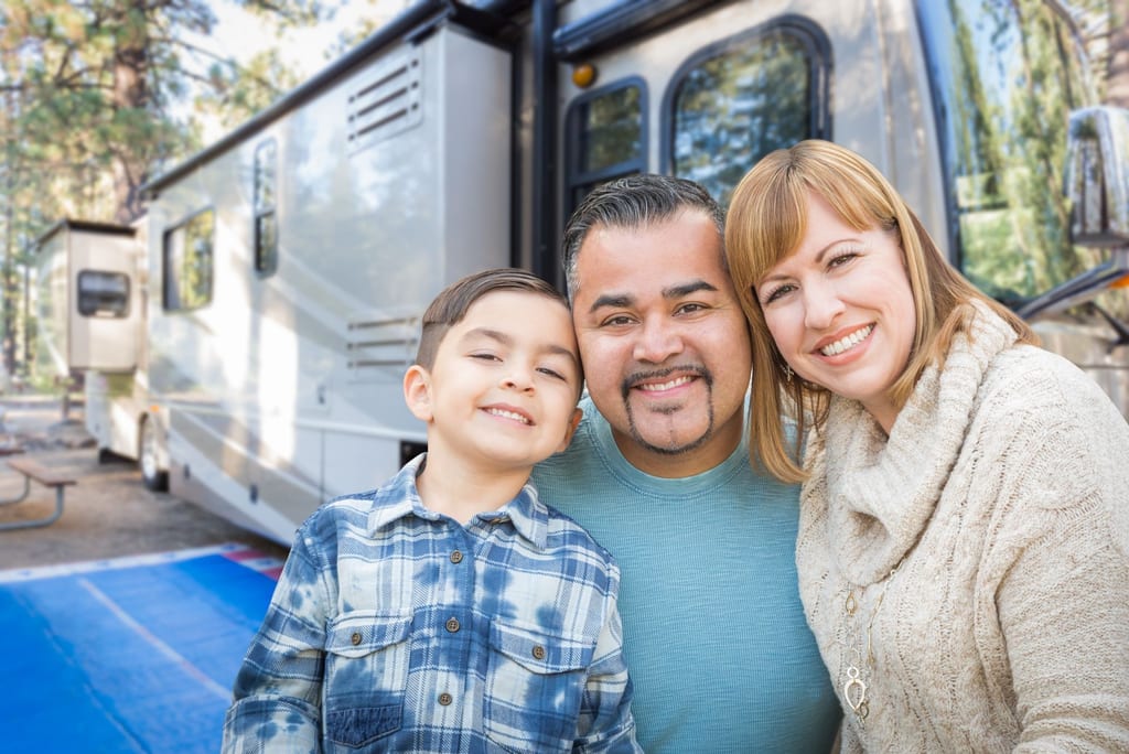 A young family standing together in front of their parked recreational vehicle.