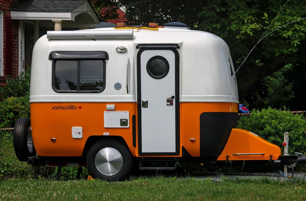 A travel trailer parked on a gravel pad beside a stand of trees.
