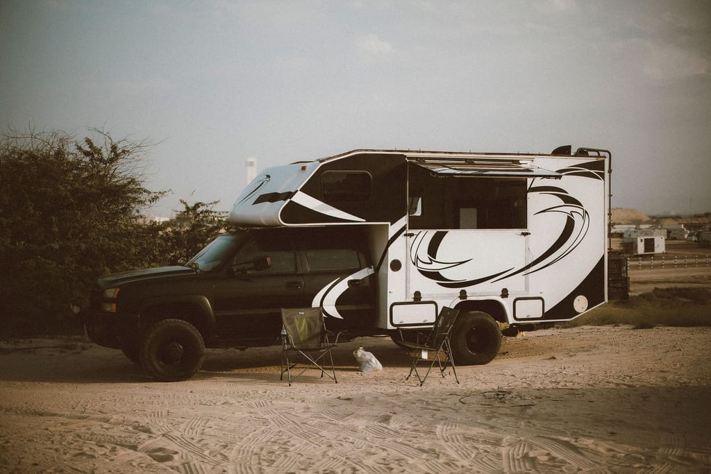 Camper truck with pop-up roof parked in a dusty lot beside a small trash bin.