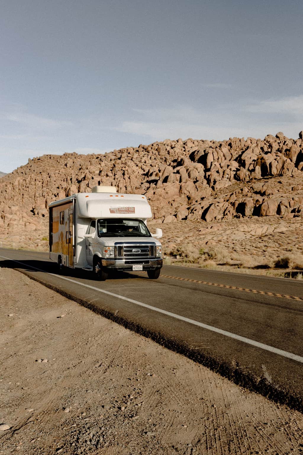 A truck on a desert road beside rocky hills.