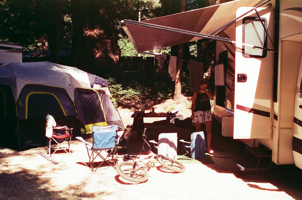 Campsite with a tent, folding chairs, and bicycles beside an RV in a wooded area