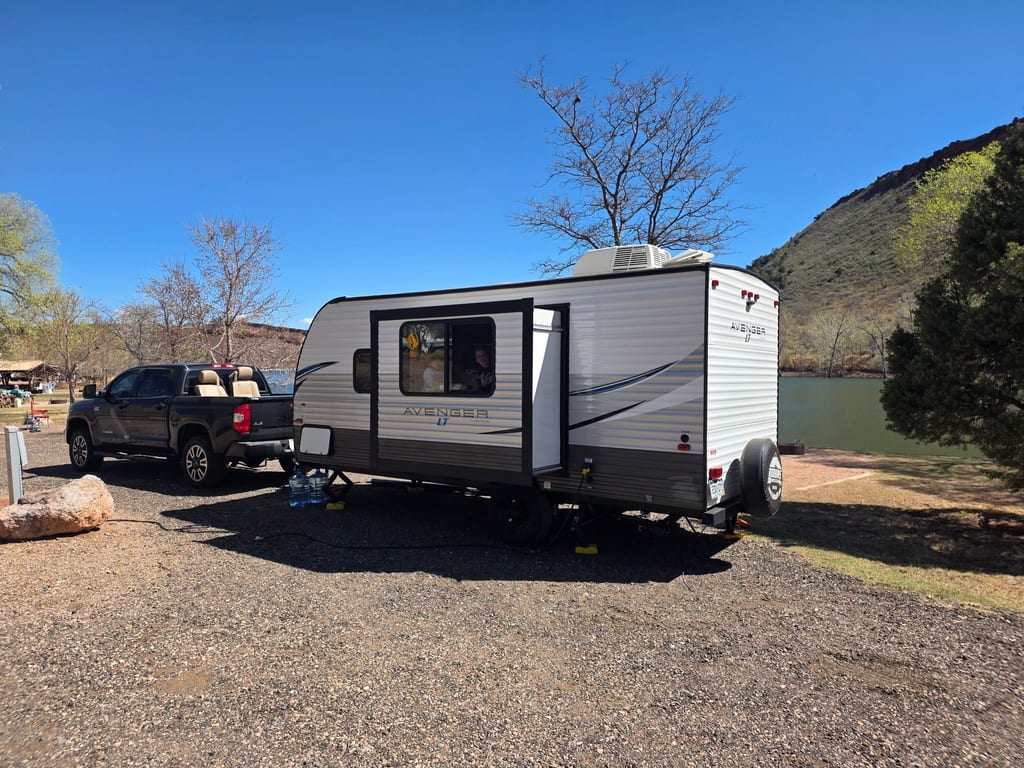 A camper set up at a wooded campsite on a bright day.